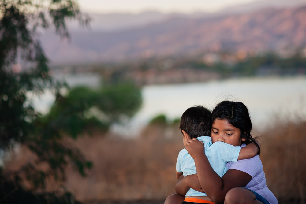 Image of a woman hugging her child near a river.