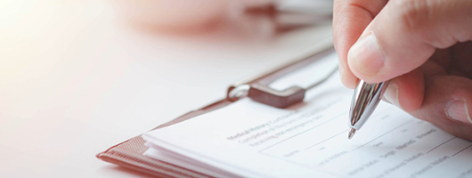 Image of a hand filling out a form with a pen on a clipboard.